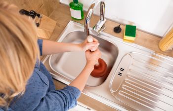 A woman unclogging a kitchen sink.