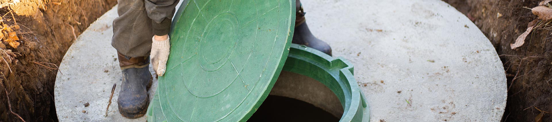 A worker removing a lid to perform a septic tank inspection.