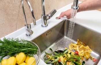 A person turning on garbage disposal to flash down vegetable peels.
