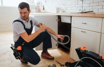 Plumber servicing clogged drain turning face away due to bad smell coming from the drain.