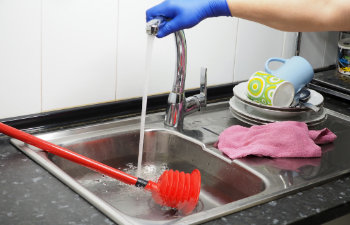 The kitchen sink full of dirty water and a red plunger