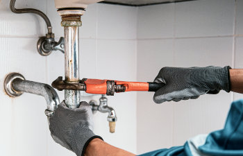 Technician plumber using a wrench to repair a water pipe under the sink