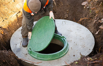 worker installs a sewer manhole on a septic tank made of concrete rings construction of sewerage