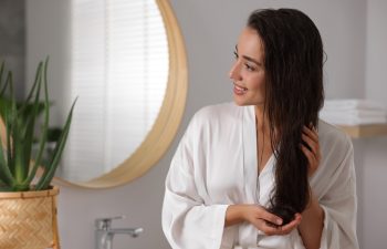Young woman applying cosmetic hair mask in bathroom. Space for text